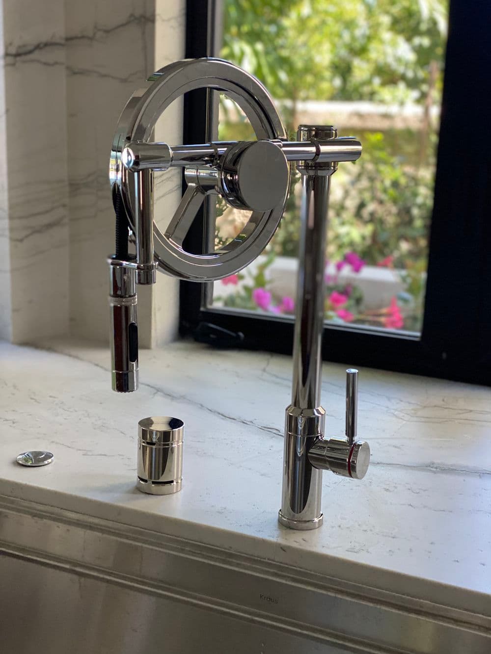 Modern chrome kitchen faucet with unique wheel design and sleek lever in a bright setting.