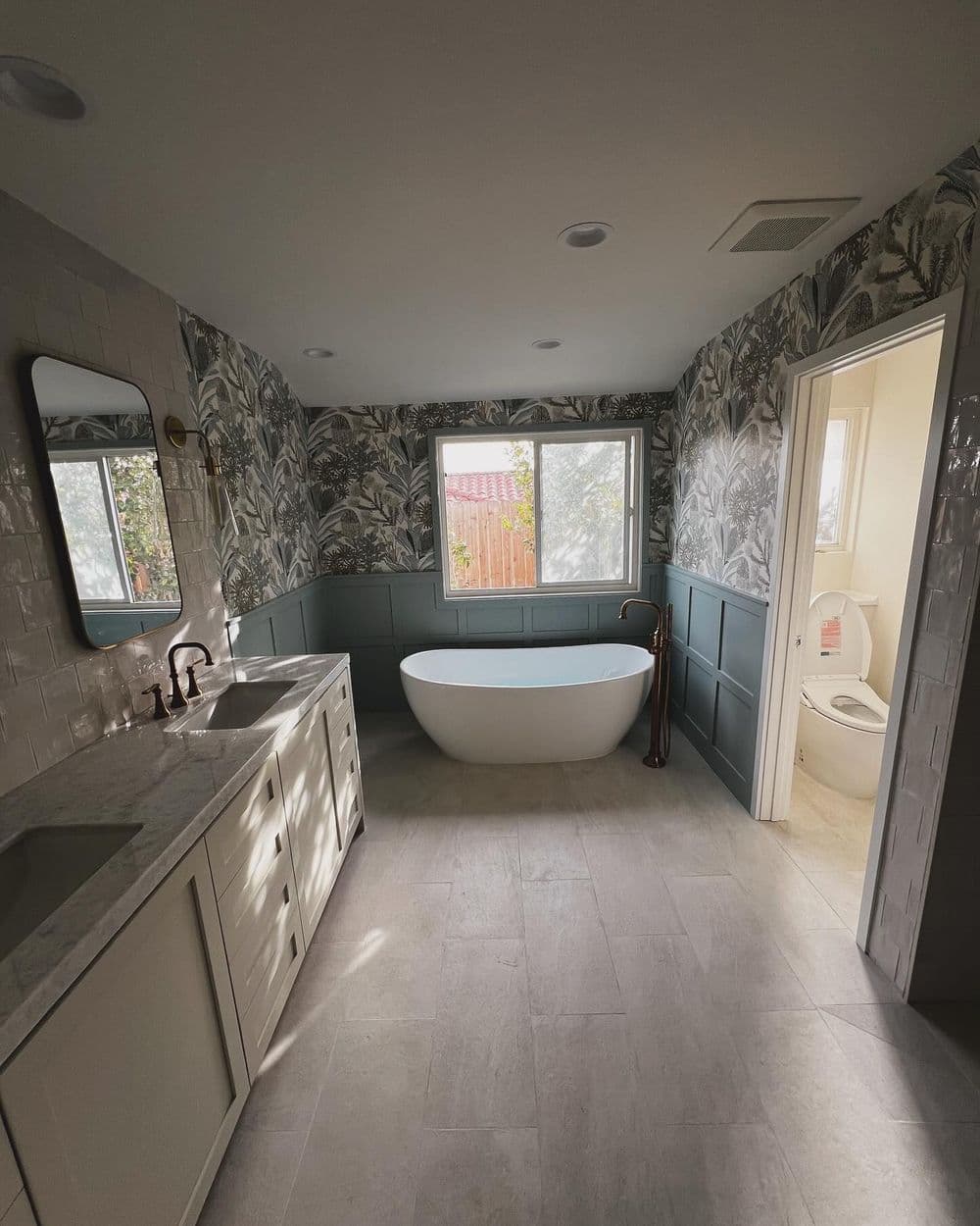 Modern bathroom with freestanding tub, white cabinetry, and botanical wallpaper. Spacious design.