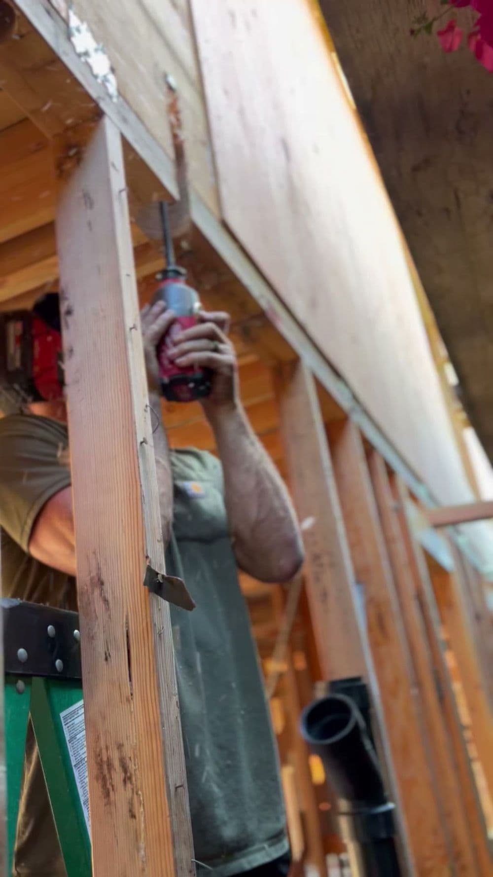 Person using a power drill while working on wood framing in a construction setting.