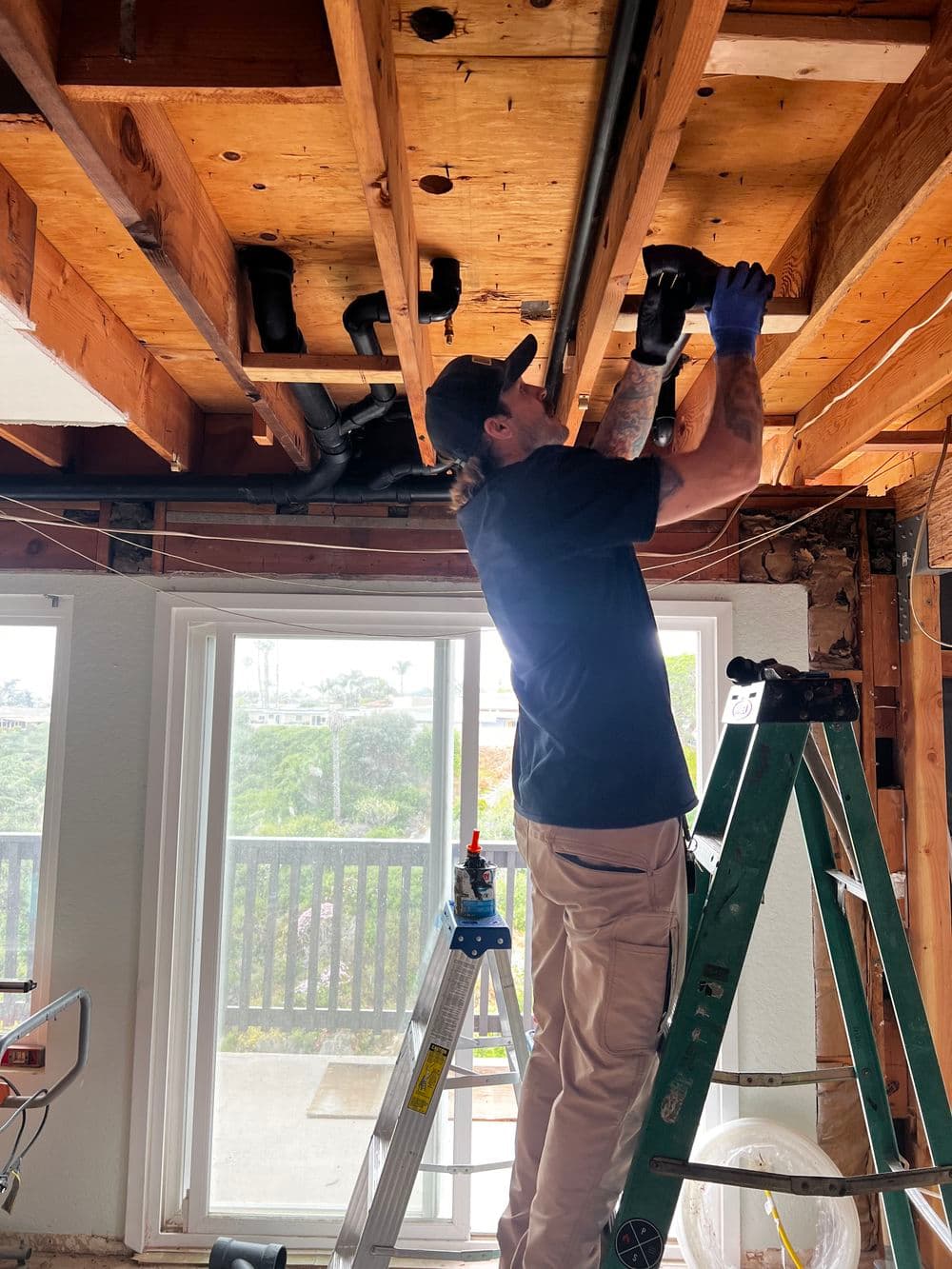 Electrician installing wiring on ceiling beams in a home renovation project.