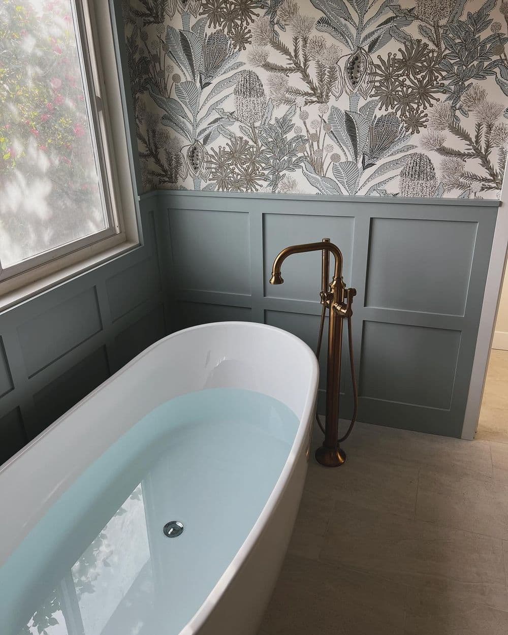 Modern bathroom with freestanding tub, elegant gold faucet, and botanical wallpaper.