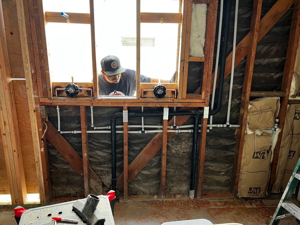 Person installing plumbing in a home renovation, visible pipes and window frame.