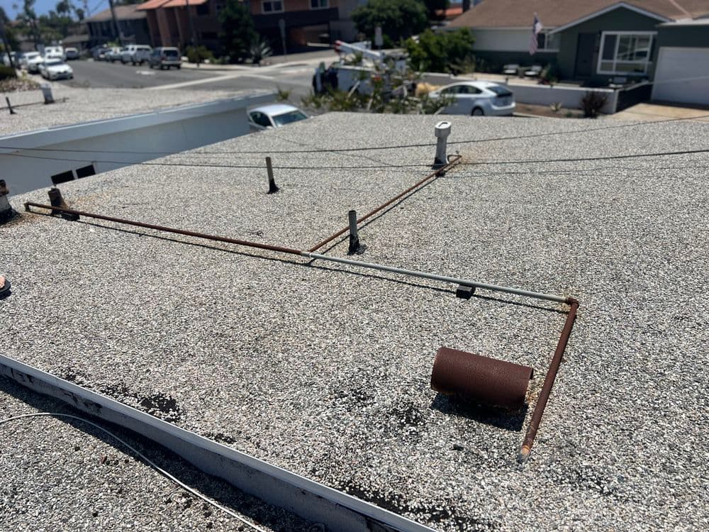 Roof installation showing pipes and gravel surface with residential area in background.
