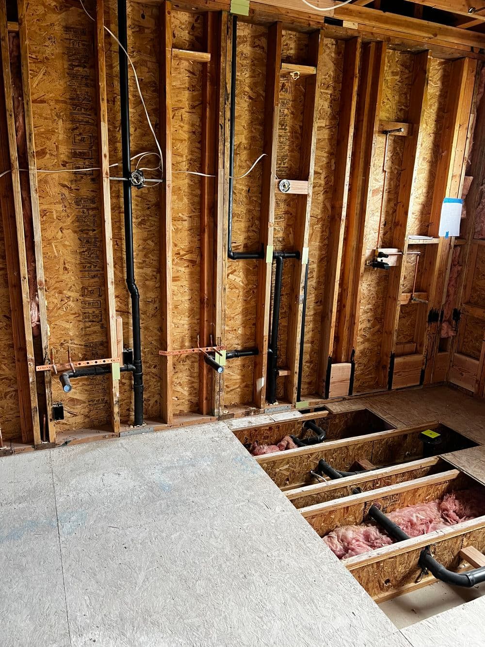 Exposed interior wall with plumbing pipes and insulation during home renovation project.