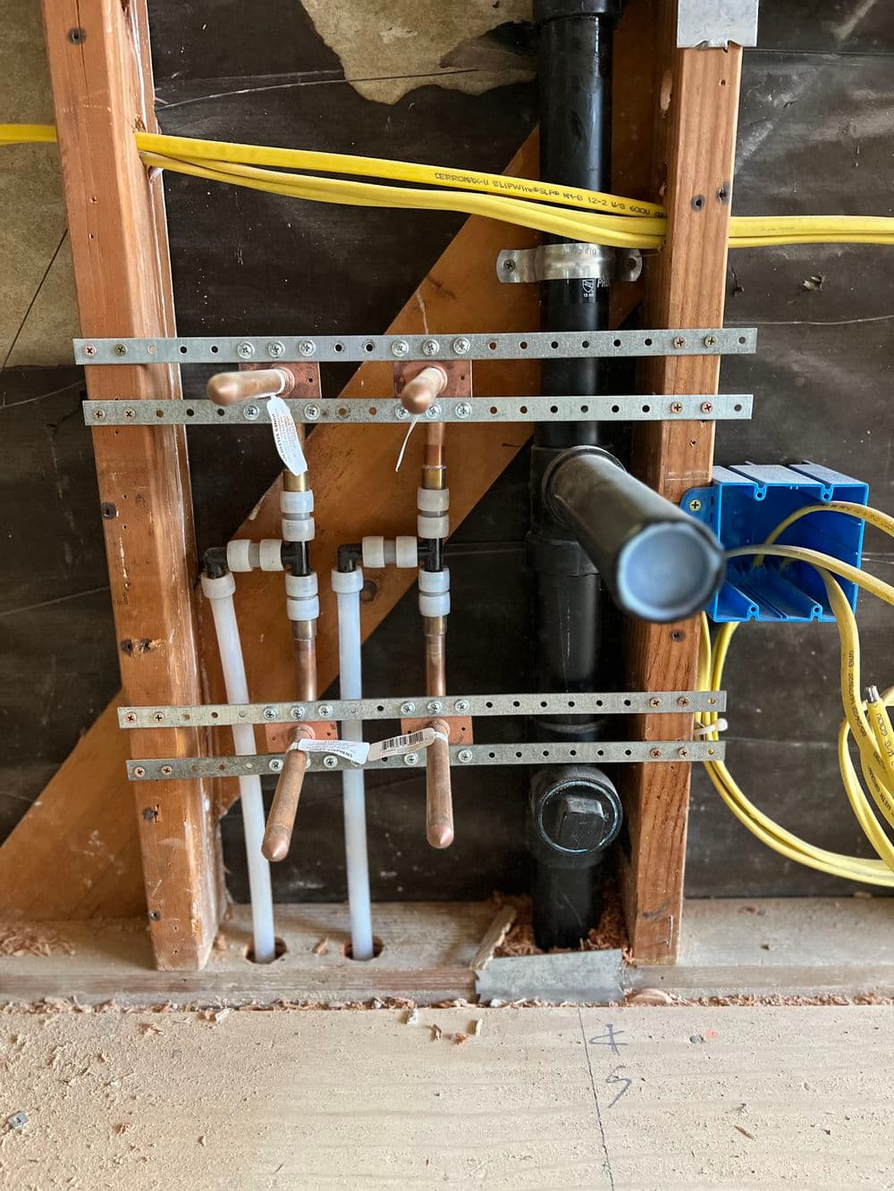 Plumbing installation with copper pipes, valves, and wiring in a home renovation project.