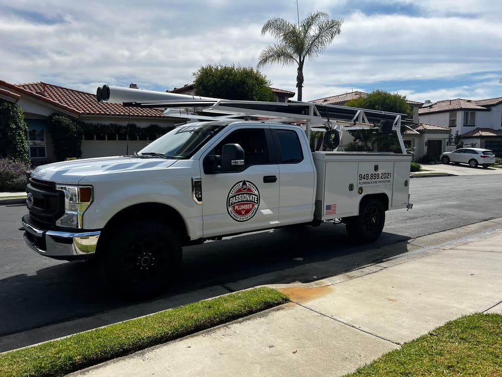 White pickup truck with ladder rack parked on residential street, featuring a logo for Passionate Plumber.