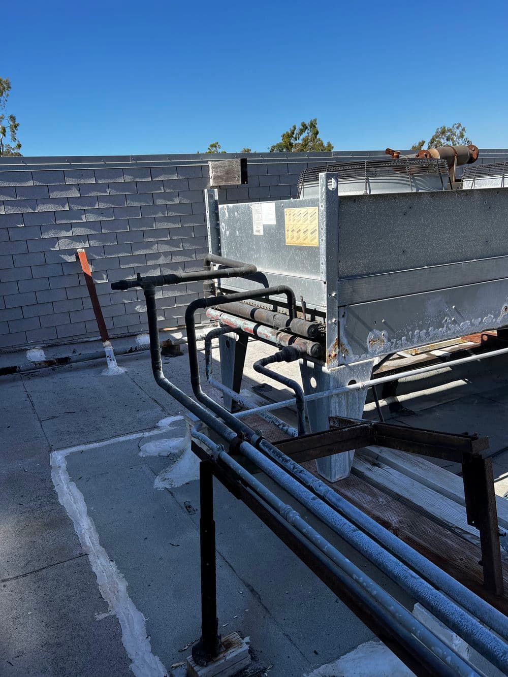 Rooftop HVAC unit with exposed piping against a clear blue sky.