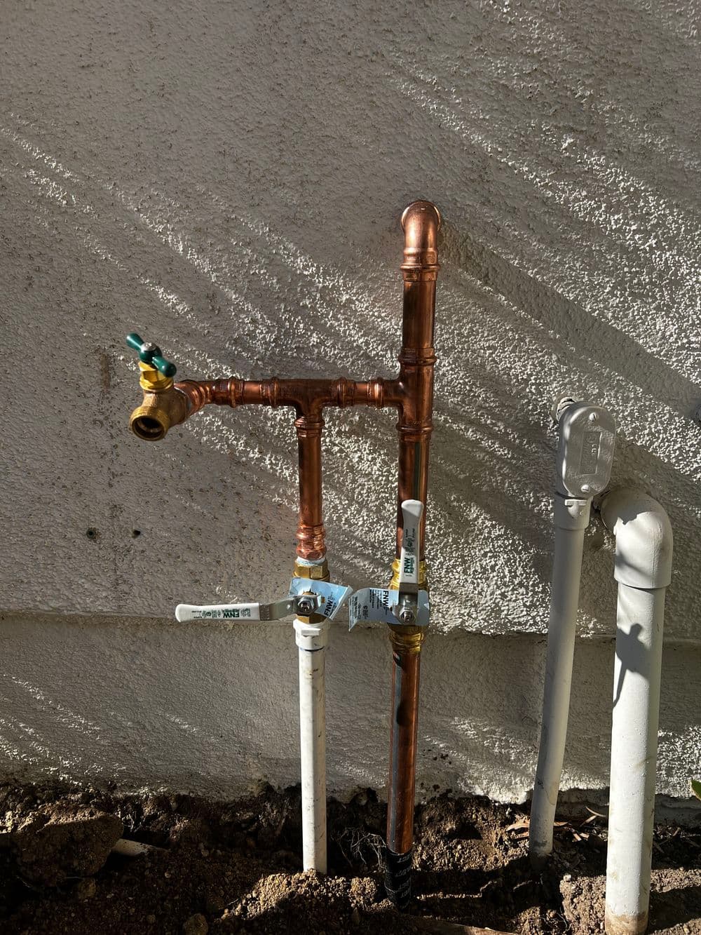 Copper plumbing pipes with valves and fittings against a textured wall.