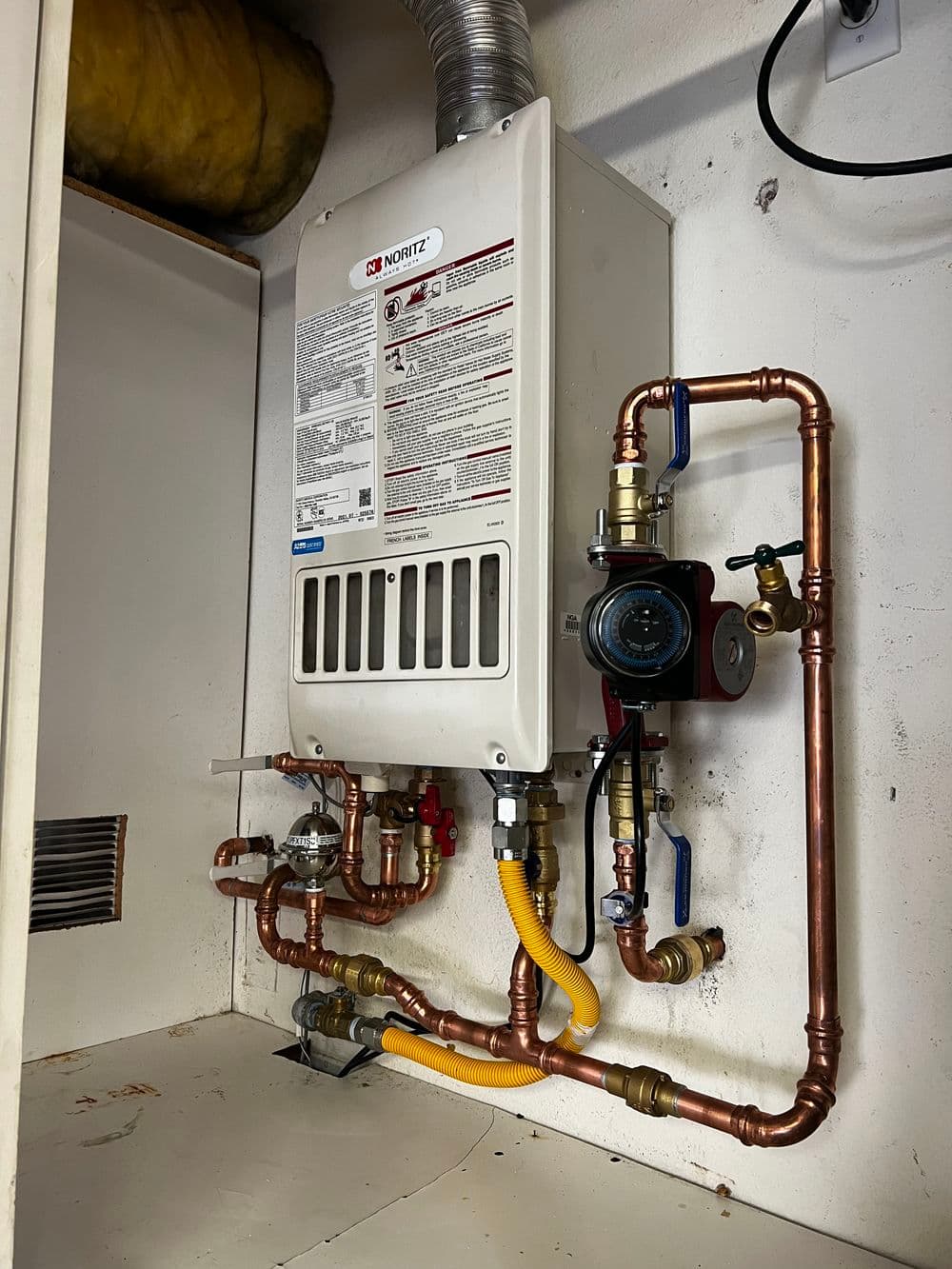 Tankless water heater installation with copper pipes and gas connections for efficient heating.
