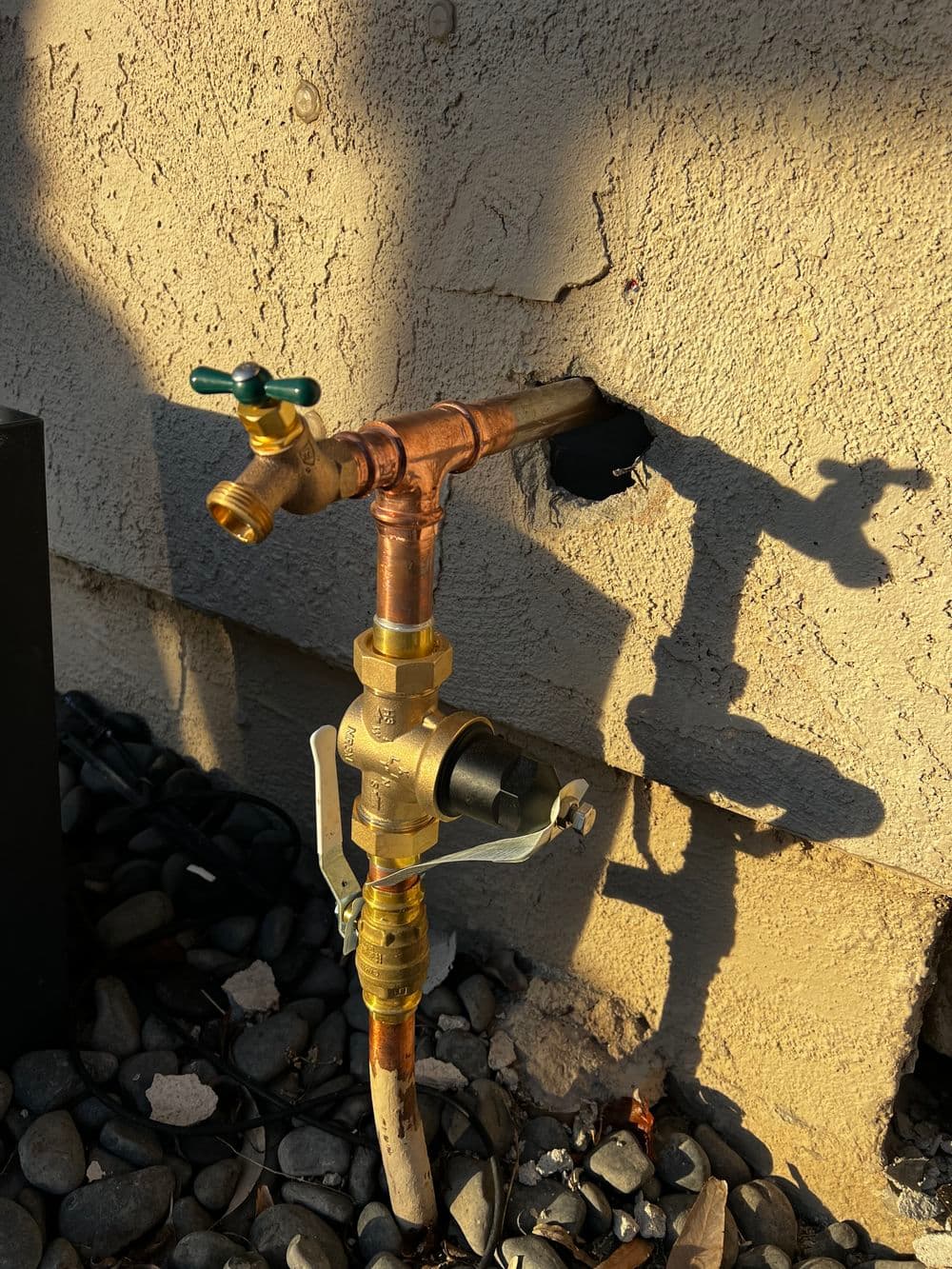 Copper water valve and pipe installation against a textured wall with a shadow.