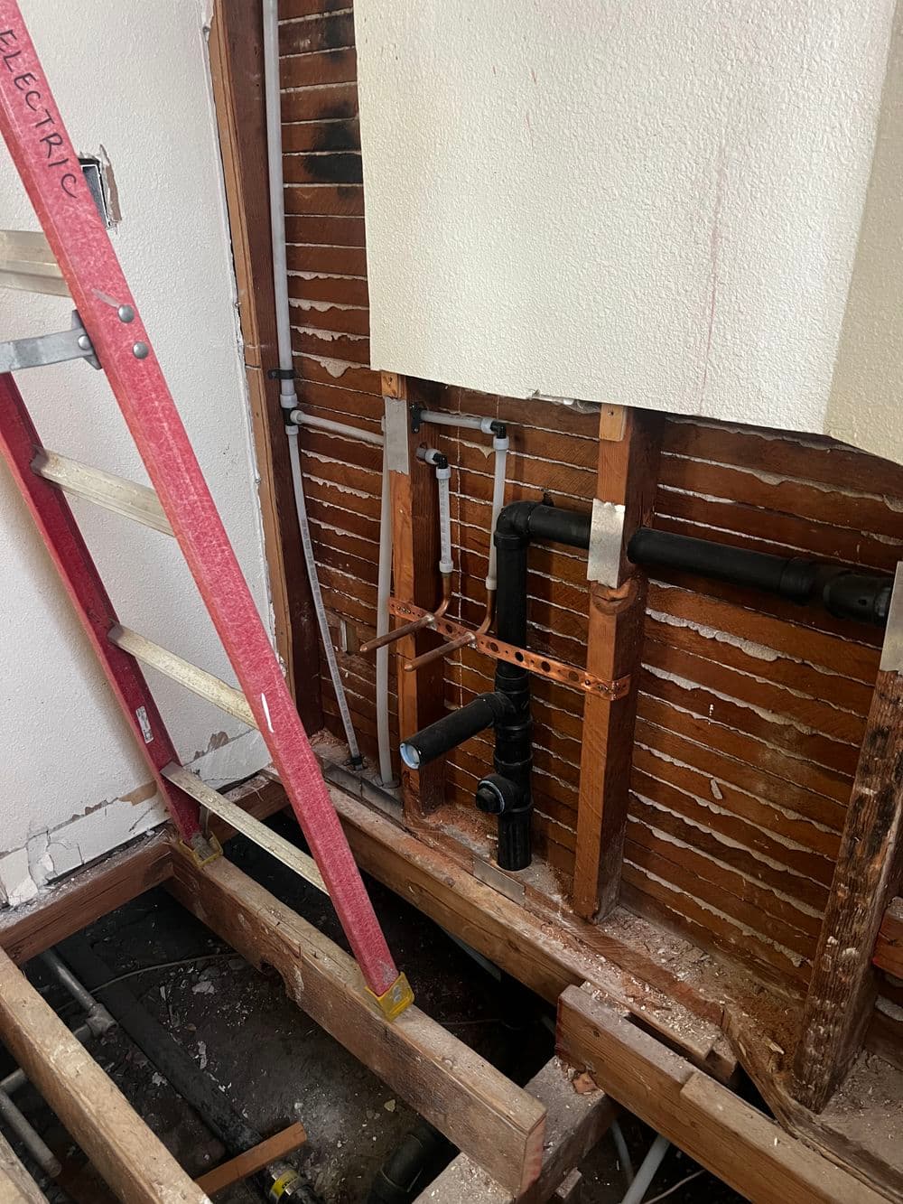 Exposed plumbing and wooden framework during home renovation with a ladder nearby.