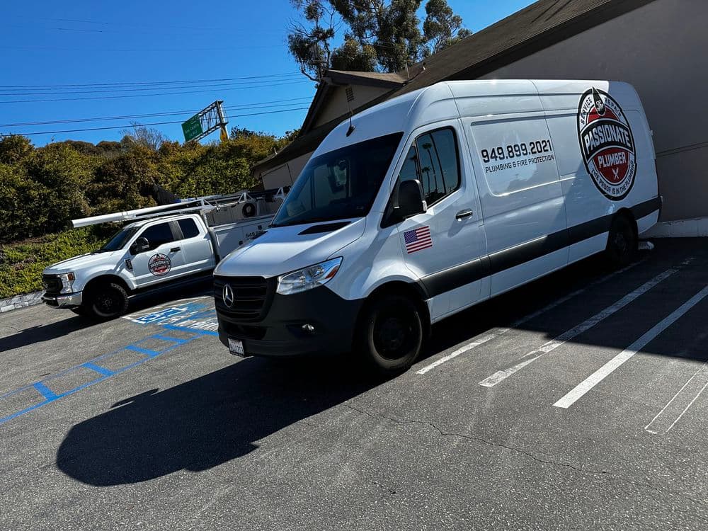 Two plumbing service vans parked outside a building, showcasing their branding and contact number.