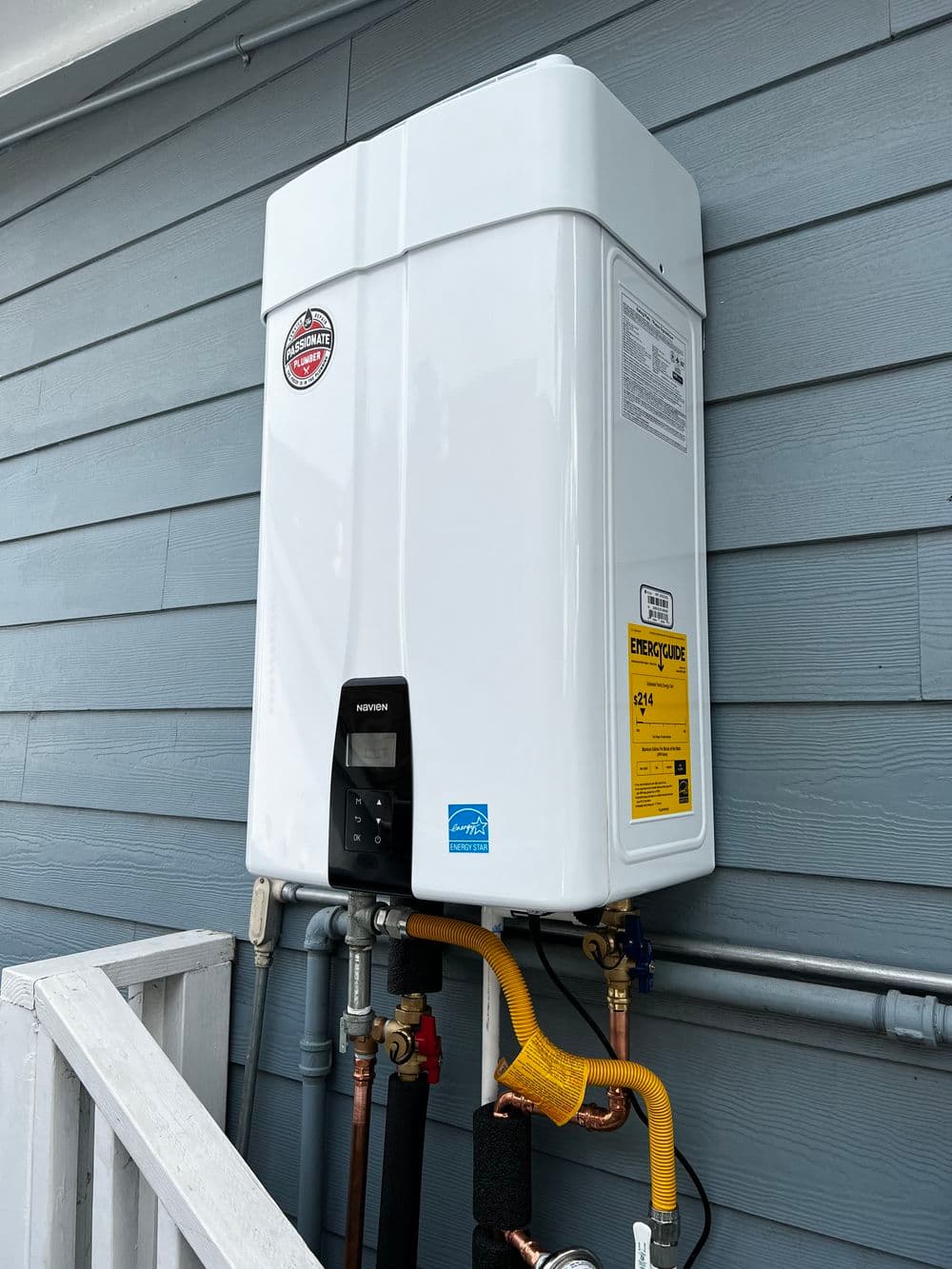 Tankless water heater mounted on a blue wooden wall with pipes and control panel visible.