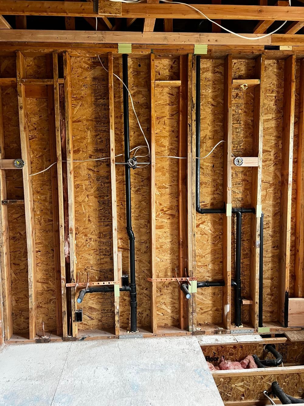 Exposed wooden wall framework with plumbing pipes for a home renovation project.