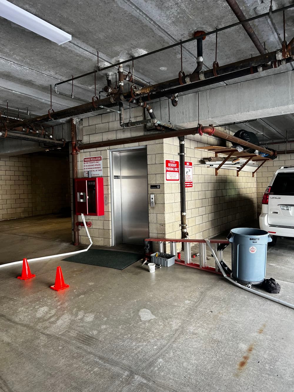 Elevator entrance in a garage with safety cones, fire control equipment, and plumbing features.