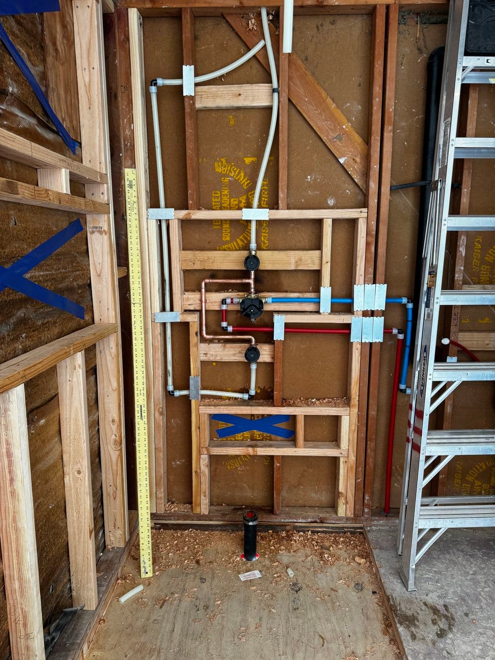 Plumbing installation framed in wall with pipes, valves, and tools in a construction setting.