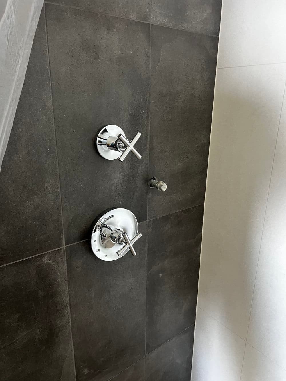 Modern shower controls on a dark tiled wall, featuring sleek chrome faucets and minimalist design.