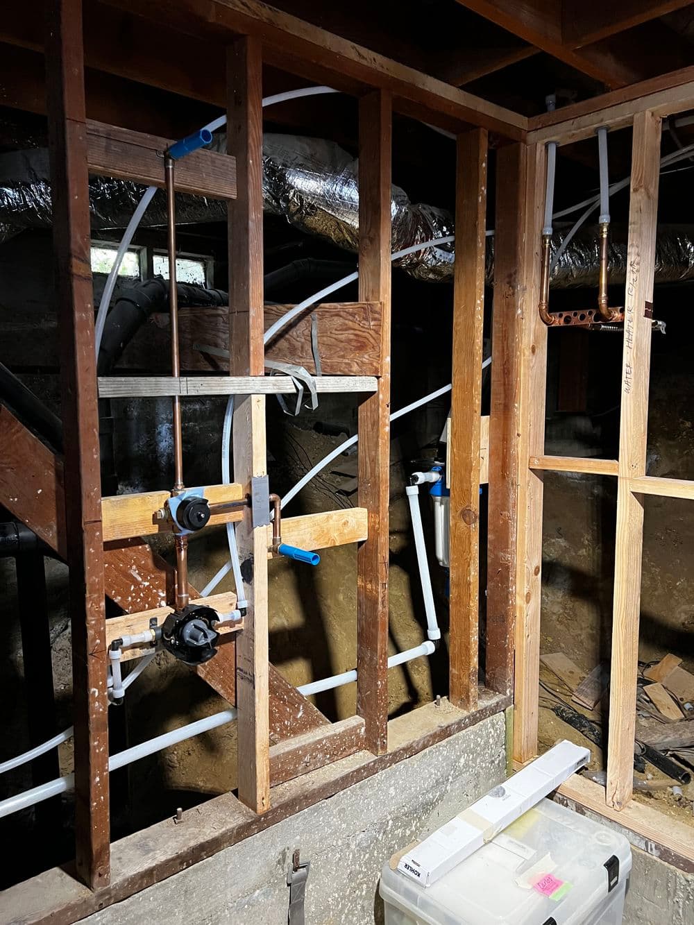 Plumbing installation with exposed pipes and framing in unfinished basement.