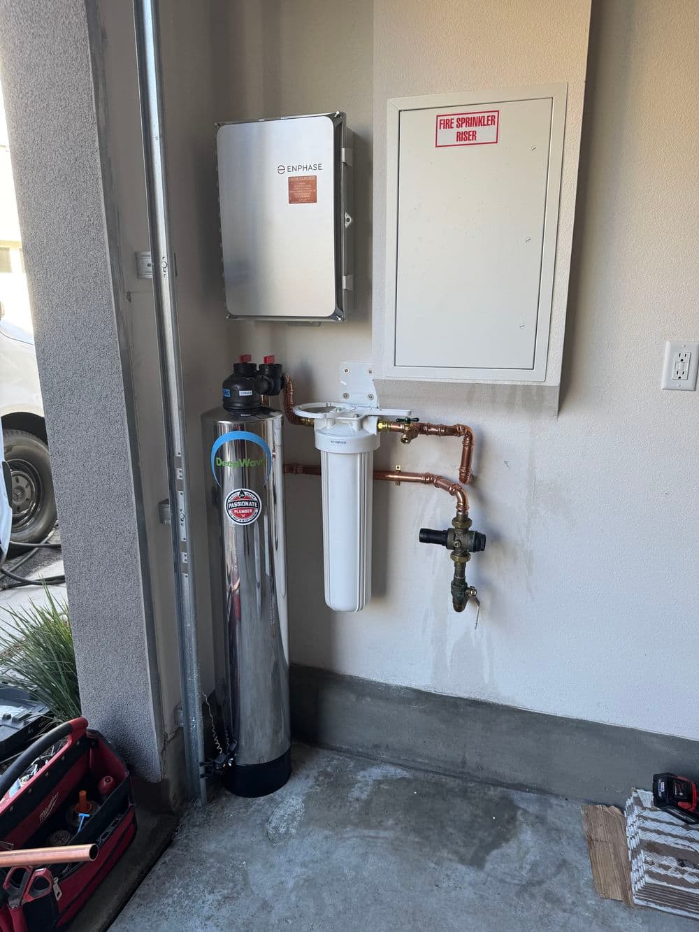 Water filtration system and electrical box installed in a garage, with plumbing connections visible.