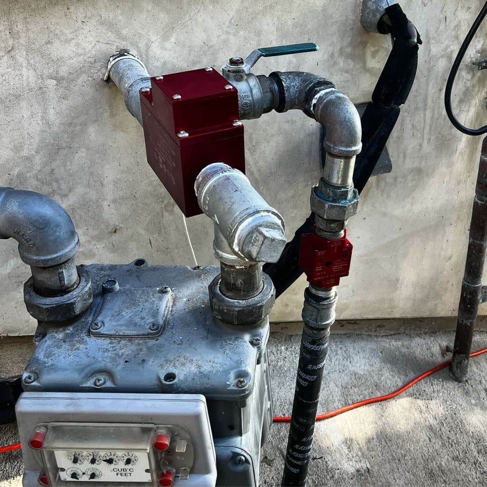 Natural gas meter with pipes and valves against a concrete wall in an outdoor setting.