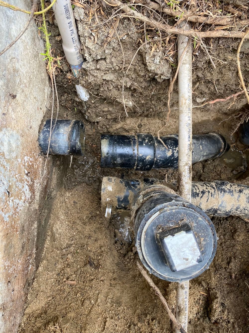 Exposed underground pipes in soil, showing connections and water leakage.