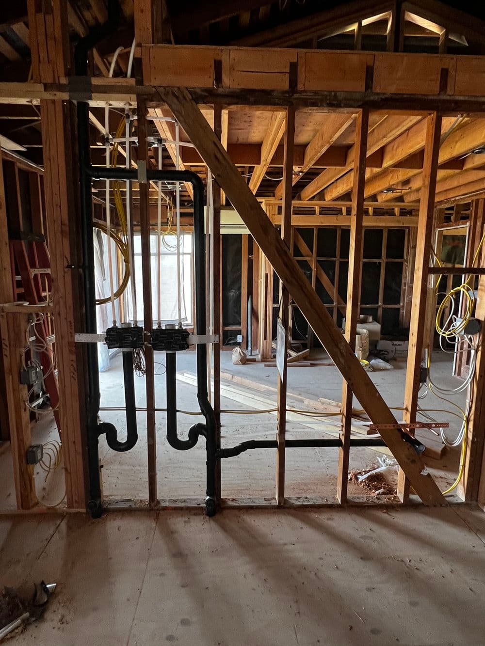 Construction site interior with exposed framing, plumbing pipes, and electrical wiring.