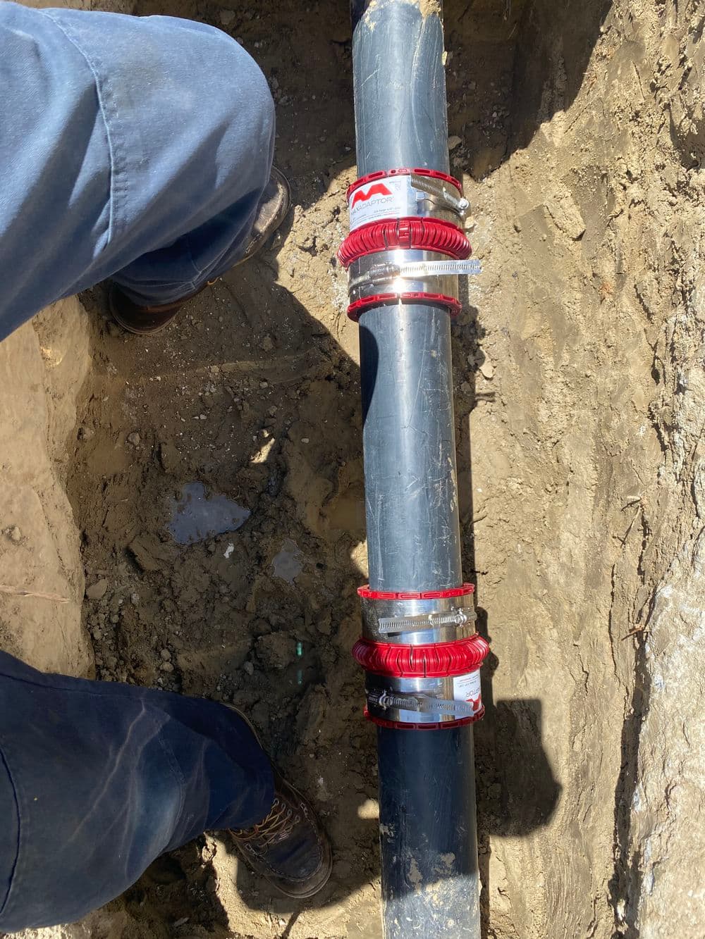Man installing red pipe fittings on a black pipe in a trench.